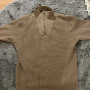 Beige ribbad tröja från Name It - Säljer en stilren beige ribbad tröja från Name It. Tröjan har en dragkedja vid halsen och långa ärmar. Perfekt för en avslappnad och bekväm stil. Den är i storlek 158-164 och för 13-14 åringar. Det är nyskick på den, använd ungefär 3 gånger innan jag ångrade mig och därför säljer jag den.