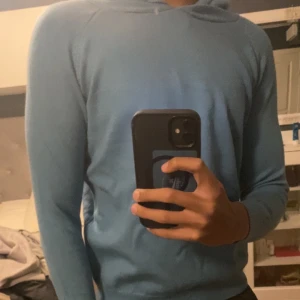 Kashmir hoodie - Säljer en stilren blå Kashmir hoodie med långa ärmar. Tröjan har ribbade muddar vid ärmslut och nederkant för en bekväm passform. Perfekt för en avslappnad look.