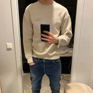  sweatshirt med logga - Säljer en stilren beige sweatshirt med en liten logga på bröstet. Riktigt fräsch och skön till våren, pris ej hugget i sten