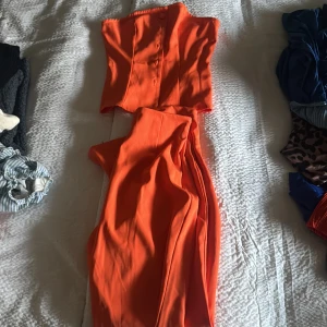 Orange axelbandslös set byxa och tröja  - Snygg orange axelbandslös set tröja och byxa med en figurnära passform. Perfekt för en somrig look med sin livfulla färg.