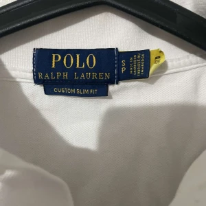 Vit pikétröja från Ralph Lauren - Säljer en klassisk vit pikétröja från Ralph Lauren i custom slim fit. Tröjan har korta ärmar och den ikoniska loggan broderad på bröstet. Perfekt för en stilren look.
