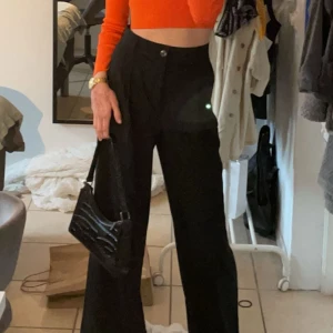 Svarta byxor från Zara - Snygga svarta byxor från Zara med hög midja och vida ben. Perfekta för en stilren look. Byxorna har en knapp och dragkedja framtill för enkel påklädning. Långa ben.