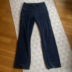 Mörkblåa byxor från Juicy Couture - Snygga mörkblåa byxor från Juicy Couture i mjukt material. Byxorna har en bekväm passform med resår i midjan och dragsko. De har också praktiska fickor både fram och bak, vilket ger en avslappnad look.