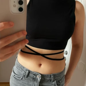 Svart ribbad topp med knytband - Säljer denna snygga svarta ribbade toppen med knytband som korsas runt midjan. 🩷