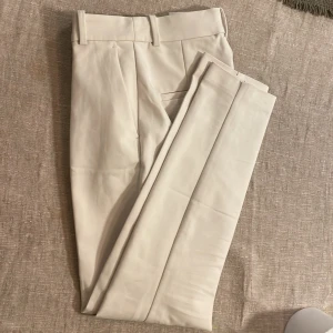 Beige kostymbyxor - Snygga vita kostymbyxor med hög midja och stilren design. Byxorna har en klassisk passform med bälteshällor och diskreta fickor. Perfekta för en elegant look. Aldrig använda. 