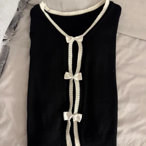 Svart kofta med vita rosetter - Säljer en elegant svart kofta med vita detaljer och tre söta rosetter framtill, koftan har långa ärmar 