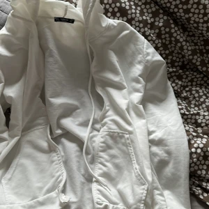 Vit hoodie S ny o fin skick - Säljer en stilren vit hoodie från H&M med dragkedja och fickor framtill. Perfekt för en avslappnad look. Den har en justerbar huva med snören.