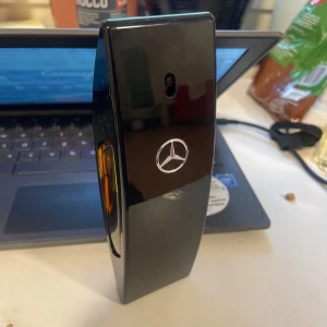 Mercedes Black Club 100ml - Snygg och elegant svart parfymflaska från Mercedes-Benz med en modern design. Flaskan har en distinkt form med en genomskinlig del som visar den gyllene vätskan inuti. Perfekt för den stilmedvetna. Ca80 ml kvar!