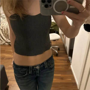 Grå korsettopp - Säljer en stilren grå korsettopp från Zara i ett snyggt fiskbensmönster. Toppen är axelbandslös och croppad, perfekt för en trendig look. Passar bra till både jeans och kjol. Perfekt för att skapa en chic outfit! 