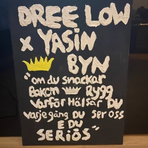 Tavla med citat av Dree Low och Yasin - En svart tavla med vit text och en gul krona. Texten är ett citat av Dree Low och Yasin, med orden 'om du snackar bakom ryggen varför hälsar du varje gång du ser oss e du seriös'. Perfekt för den som gillar svensk hiphop och vill ha något unikt på väggen.                           PRIS GÅR ATT DISKUTERAS VID SNABBA AFÄRER