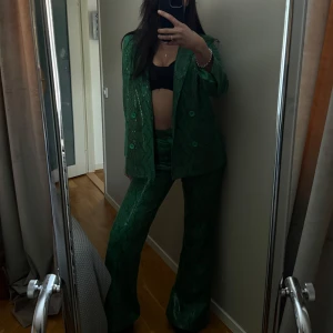 STAND STUDIO - Snygg grön orm mönstrad kostym med kavaj och byxor. Kavajen har dubbelknäppning och byxorna är raka. Perfekt för en trendig look. Endast använd en gång. Ord pris 4.999