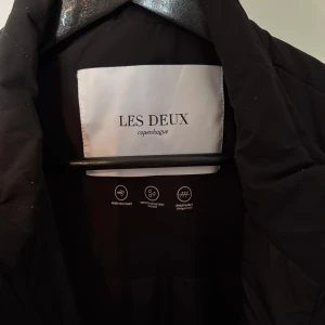 Svart väst från Les Deux - Snygg svart puffer väst från Les Deux med praktiska fickor och dragkedja. Modell Maxwell Water resistent vest. Perfekt för lager-på-lager stil. Västen har en modern design med mesh-detaljer på ena sidan. Väldigt fint skick, knappt använd. Storlek XL. Nypris ca 2000kr