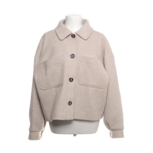 Beige jacka från NA-KD - Säljer en stilren beige jacka från NA-KD. Jackan har en oversized passform med stora knappar och två stora fickor framtill. Den är långärmad och har en klassisk krage. Perfekt för en trendig look!