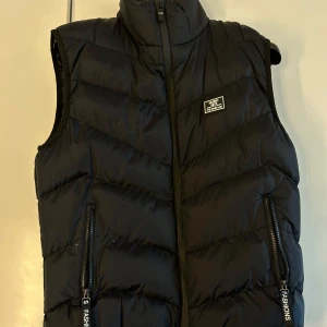 Svart dunväst med dragkedja - Snygg svart dunväst med dragkedja framtill och två praktiska fickor med dragkedjor. 