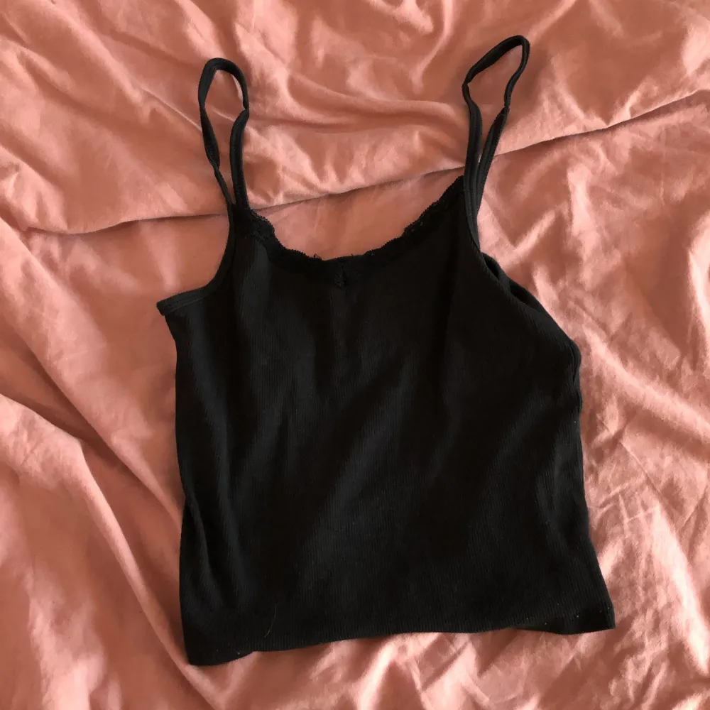 Säljer en svart ribbad linnetopp från H&M med spetsdetaljer vid halsringningen. Perfekt för en stilren look. Toppen har smala axelband och är tillverkad i ett mjukt material.. Yläosat.