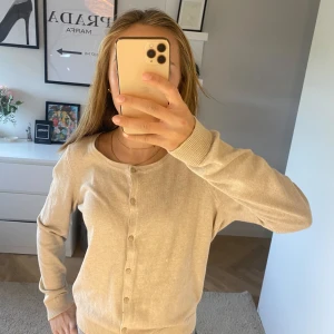 Beige kofta från H&M - Säljer en stilren beige kofta från H&M. Den har långa ärmar och knappar framtill. Perfekt för en avslappnad look. Passar bra till både jeans och kjol.
