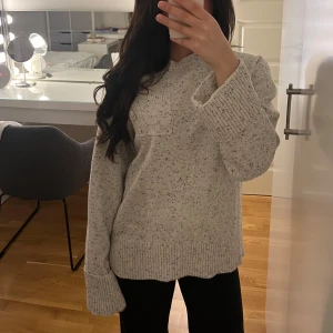 Grå stickad tröja med ficka - Mysig grå stickad tröja med en liten ficka på bröstet. Tröjan har långa ärmar och ribbade kanter vid ärmslut och nederkant. Perfekt för kyliga dagar!