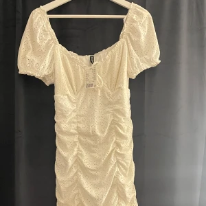 STUDENT klänning med puffärmar - Charmig vit klänning med korta puffärmar och rynkad design. Klänningen har ett broderat mönster och en söt, romantisk stil. Perfekt för sommarens alla tillfällen och även studenten. HELT NY aldrig använt. Prislapp kvar 