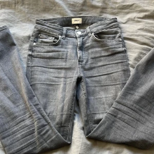Grå jeans från ONLY - Snygga grå jeans från ONLY i en klassisk femficksmodell. De har en knapp och dragkedja framtill och är tillverkade i ett bekvämt denimtyg. Perfekta för en avslappnad stil.