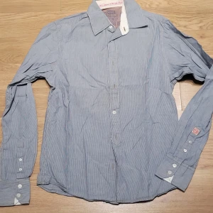 Randig skjorta från Scotch & Soda - Säljer en snygg randig skjorta från Scotch & Soda i blått och vitt. Skjortan har långa ärmar och knappar framtill. Perfekt för både vardag och fest! Den är i bra skick och passar perfekt till höst och vår.