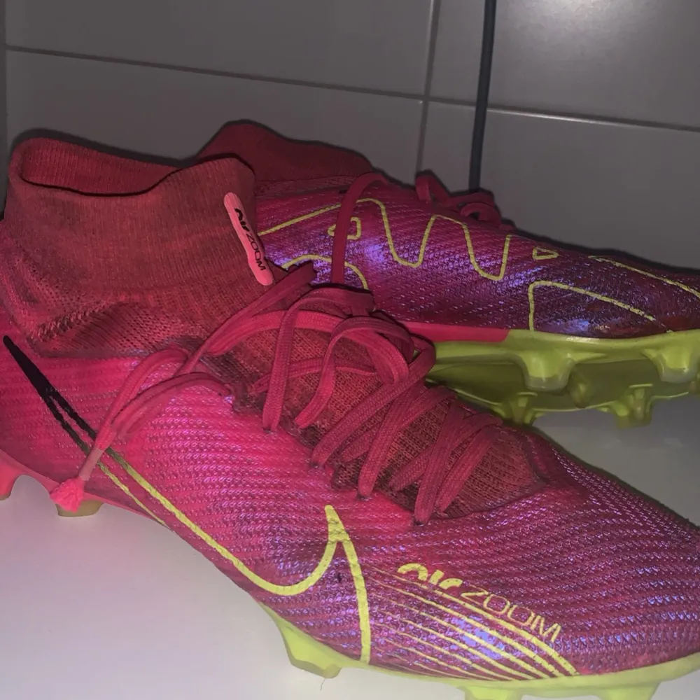 Säljer ett par Nike Mercurial fotbollsskor i en cool rosa färg med gula detaljer. Skorna har snörning och är i syntetmaterial, perfekt för fotbollsträning. De har en tight passform och är i mycket bra skick. Sulan är designad för optimalt grepp på planen.. Skor.