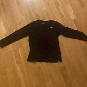 Svart långärmad tröja från Levi's - Säljer en svart långärmad tröja från Levi's i mycket bra skick. Tröjan är ribbad och har en liten röd Levi's-logga på bröstet. Perfekt för höst och vinter, och passar till både vardag och fest. Skön och stilren design!