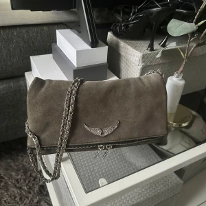 Zadig & Voltaire väska suede - Grå suede zadig voltaire väska, äkta! Har haft i några år och är använd men har inga märkbara defekter. Alla stenar är kvar på zadig märket. Önskas fler och närmre bilder kan man skriva så löser jag direkt!🥰
