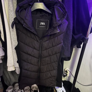 Svart pufferjacka från Zara - Säljer en svart pufferväst från Zara i storlek M. Jackan har en dragkedja framtill och en mysig huva. Perfekt för kyliga dagar och ger en stilren look. Använd ett fåtal gånger, så den är i mycket bra skick. Passar perfekt till höst och vinter!