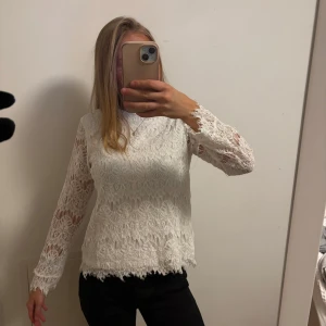 Vit spetsblus - Säljer en superfin vit spetsblus med långa ärmar. Perfekt för både vardag och fest! Blusen har ett vackert blommigt mönster och är i mycket bra skick. Den är både elegant och bekväm, och passar perfekt till ett par jeans eller en kjol.