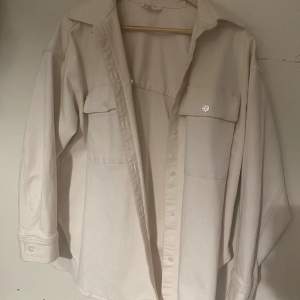 Säljer en snygg beige overshirt i storlek M. Den har långa ärmar och två stora fickor framtill. Perfekt för lager-på-lager under höst och vår. Skjortan är i bra skick och har en klassisk krage med knappar hela vägen ner. Passar både till vardags och lite mer uppklädda tillfällen.