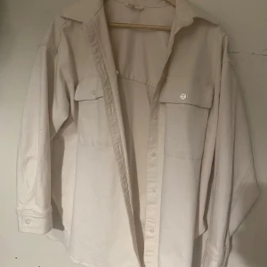 Beige overshirt med fickor - Säljer en snygg beige overshirt i storlek M. Den har långa ärmar och två stora fickor framtill. Perfekt för lager-på-lager under höst och vår. Skjortan är i bra skick och har en klassisk krage med knappar hela vägen ner. Passar både till vardags och lite mer uppklädda tillfällen.