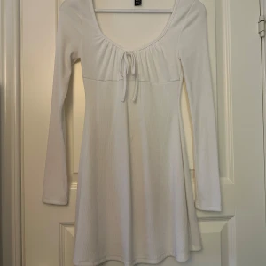 Vit långärmad klänning - Säljer en superfin vit långärmad klänning i mjukt material. Den har en söt knytning framtill och en bekväm passform som passar perfekt till både student och skolavslutning. Klänningen är i mycket bra skick och aldrig andvänd.