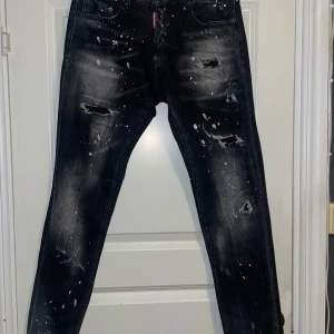 Svarta jeans från Dsquared2 - Säljer ett par svarta Dsquared2 jeans i slim fit. De har en cool distressed look med färgstänk och slitningar som ger en edgy stil. Perfekta för både vardag och fest.
