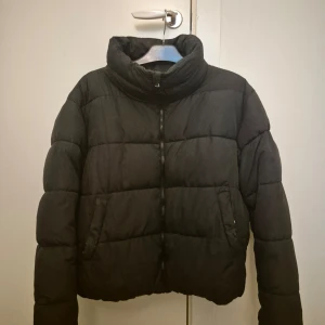 Svart pufferjacka från Lager 157 - Säljer en svart pufferjacka från 157 i storlek M. Jackan har en hög krage och dragkedja framtill. Perfekt för kalla dagar med sin vadderade design. Den är i bra skick och varit väl omhändertagen.