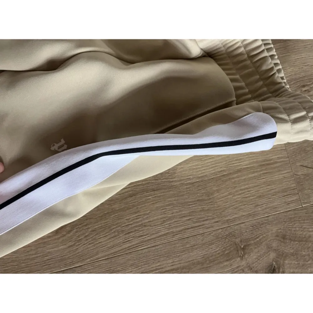 Beige träningsbyxor från Palm Angels. De har en elastisk midja och vita . Köpte för nån vecka sen men dem passa inte min storlek . Farkut & Housut.