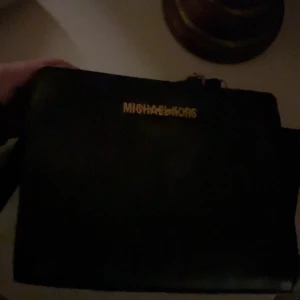 Svart axelväska från Michael Kors - Snygg svart axelväska från Michael Kors i skinn. Väskan har en praktisk dragkedja och ett stilrent foder med MK-logga. Perfekt för både vardag och fest!