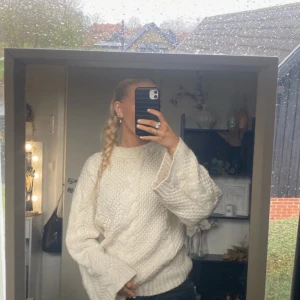 Vit stickad tröja - Mysig vit stickad tröja med kabelstickat mönster. Perfekt för kyliga dagar med sin varma och bekväma passform. Tröjan har långa ärmar och en avslappnad stil som passar både till vardags och mysiga hemmakvällar. Lite Oversized i strl