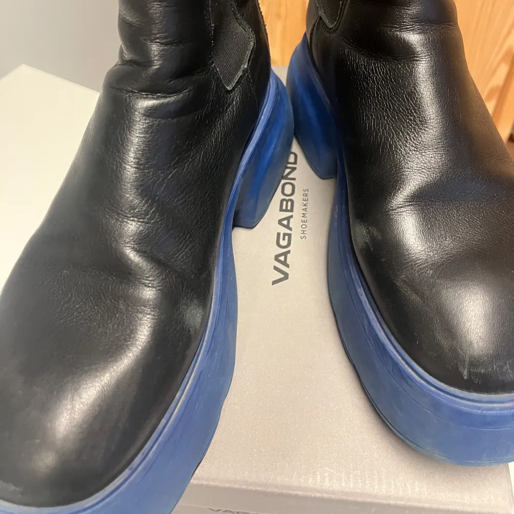 Säljer ett par coola svarta boots i skinn från CPNHGN med en chunky blå sula. De har en stilren design med elastiska paneler på sidorna för enkel på- och avtagning. Perfekta för att ge din outfit en edgy touch! 🖤💙. Skor.