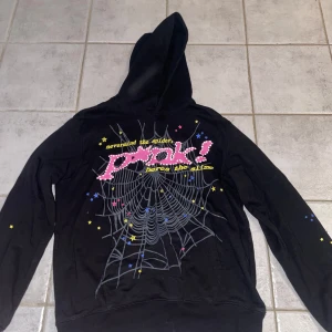Svart hoodie från Sp5der - Cool svart hoodie från Sp5der med ett stort spindelnätsmönster och texten 'Nevermind the spider, here's the slime' på baksidan. Den har en stjärnlogga på framsidan och är gjord av 100% bomull. Perfekt för en avslappnad stil!