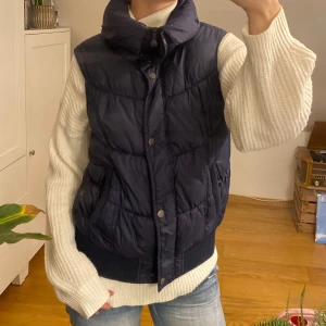Mörkblå dunväst från Clockhouse - Säljer en snygg och varm mörkblå dunväst från Clockhouse. Västen har knappar framtill och en hög krage som skyddar mot kyla. Perfekt för höst och vinter!🎀