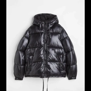 Svart pufferjacka med luva  - Säljer en snygg svart pufferjacka med glansig yta och luva. Jackan har dragkedja framtill och perfekt för kalla dagar!. Knappt använd och i bra skick! Skriv för fler bilder!