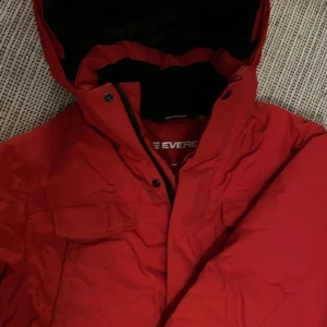 Röd vinterjacka från Everest 164 el S/M dam  - Säljer en varm och snygg röd vinterjacka från Everest. Jackan har en praktisk dragkedja och knappar framtill, perfekt för kalla dagar. Den har en skön huva och är i mycket bra skick. Perfekt för vinterns alla äventyr! ❄️Strlk 164 el S/M dam