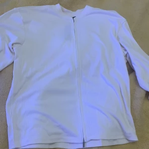  ribbad kofta - Säljer en stilren vit ribbad kofta med dragkedja framtill. Perfekt för finare middagar/jobbe eller utekväll.  Den har en enkel design med långa ärmar och rund hals. Passar både till vardags och lite finare tillfällen. Aldrig använd för stor 