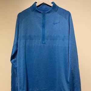Blå långärmad tröja från Nike - Säljer en snygg blå långärmad tröja från Nike. Perfekt för träning eller vardagsbruk. Tröjan har en halv dragkedja framtill och en diskret Nike-logga på bröstet. Unisex.