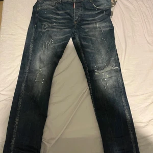 Jeans Dsquared2 - Säljer ett par snygga jeans från Dsquared2 i storlek 52. De är mörkblå med slitna detaljer och en cool, avslappnad look. Perfekta för både vardag och fest! Tillverkade i Italien med hög kvalitet. Dem passar mig och är 185 cm lång och sitter inte tight och inte baggy.