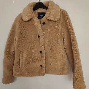 Supermysig beige teddyjacka från ONLY i storlek M. Perfekt för höst och vinter med sina långa ärmar och knappar framtill. Jackan är i mycket bra skick och har en klassisk krage som ger en stilren look. Perfekt för att hålla sig varm och snygg under kyliga dagar! 