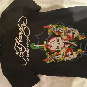 Svart Ed Hardy t-shirt med dödskallemotiv - Svart Ed Hardy t-shirt med dödskallemotiv och rhinestones. Designen är av Christian Audigier och har en spindelnätsdetalj på baksidan! passar mig som har storlek S.