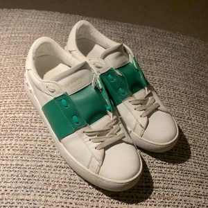 Valentino sneakers med gröna detaljer - Säljer ett par snygga Valentino sneakers i vitt skinn med gröna detaljer. De är använda men i gott skick. Jag har tvättat de som ni ser på bilderna, endast i Norrköping!!!
