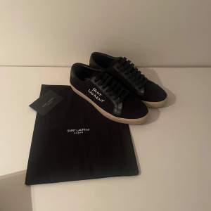 Snygga svarta sneakers från Saint Laurent i nytt skick. De har en stilren design med vit logga på sidan och svarta snören. Perfekta för både vardag och fest! Kommer med originalpåse.