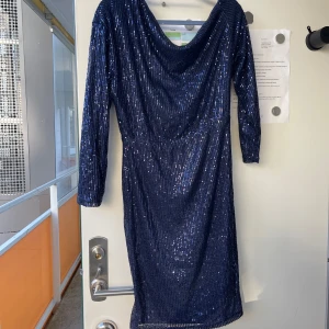 Mörkblå glittrig klänning - Snygg mörkblå klänning med glittriga paljetter över hela tyget. Den har en elegant  design och trekvartsärmar, perfekt för festliga tillfällen. Klänningen är helt ny  och passar perfekt till nyår eller andra festliga tillfällen.